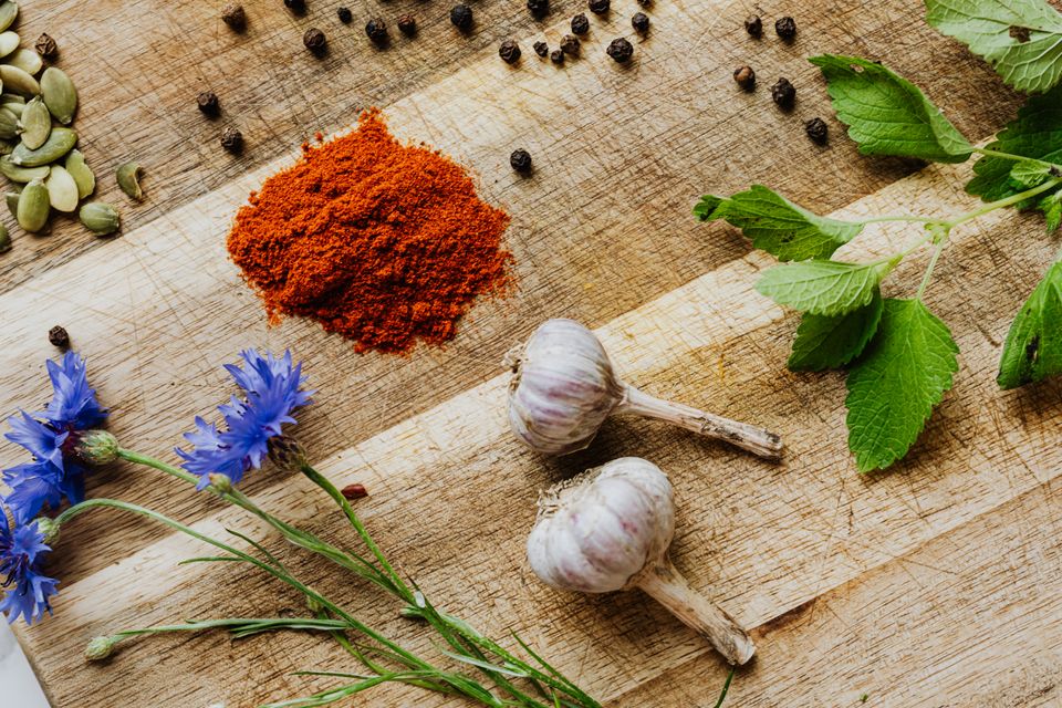 Fresh herbs, garlic, paprika, peppercorns, and flowers on a warm wooden table